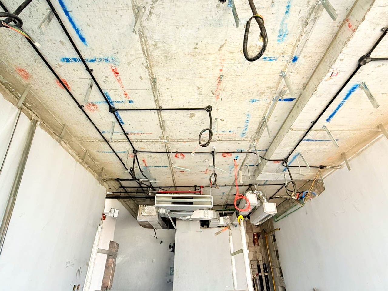 Beach Walk Iii By Imtiaz A view of a construction site ceiling with visible pipes, ductwork, and mounting fixtures against a concrete surface.